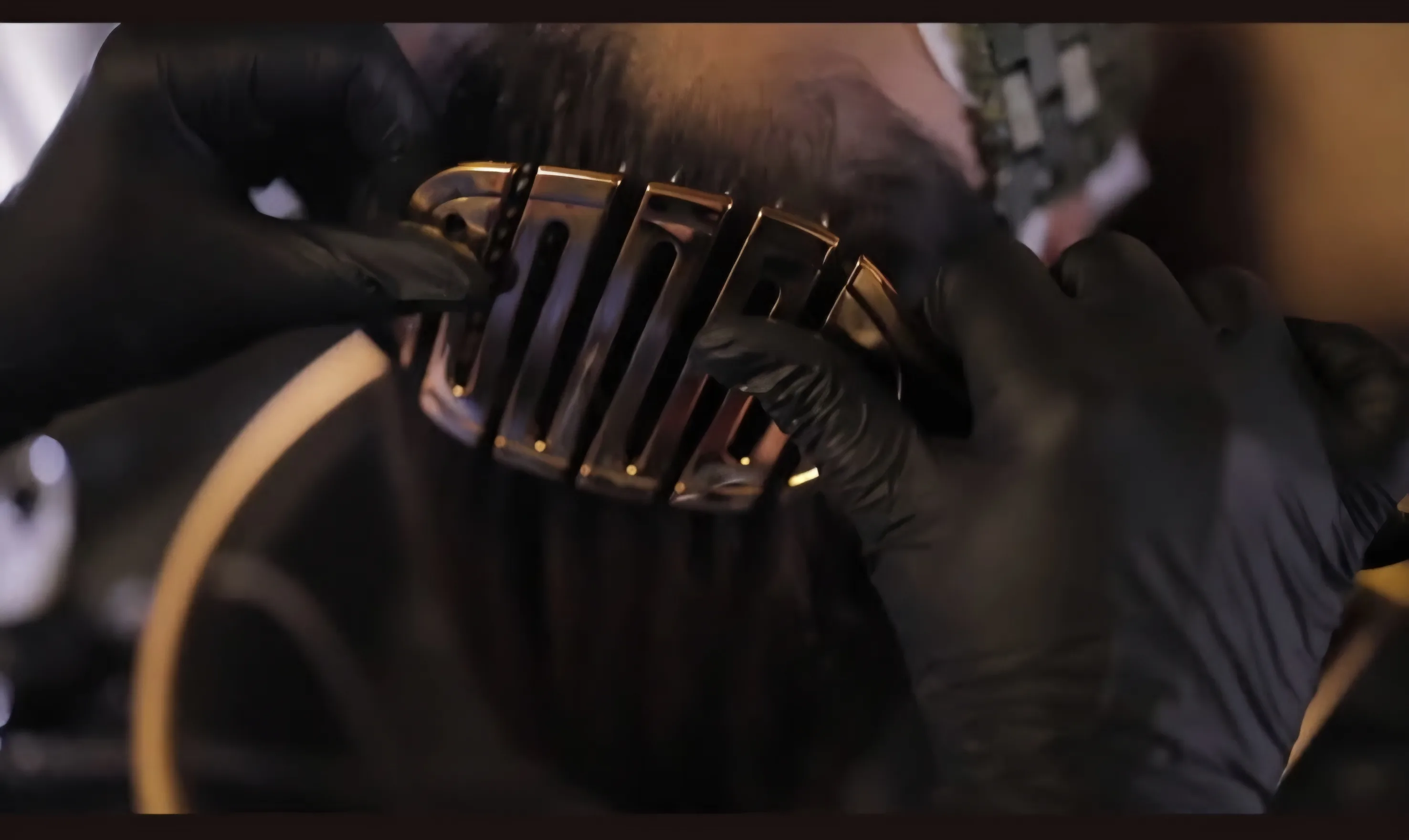 A polished brass scalp tool drawn through hair by gloved hands — precise, considered technique