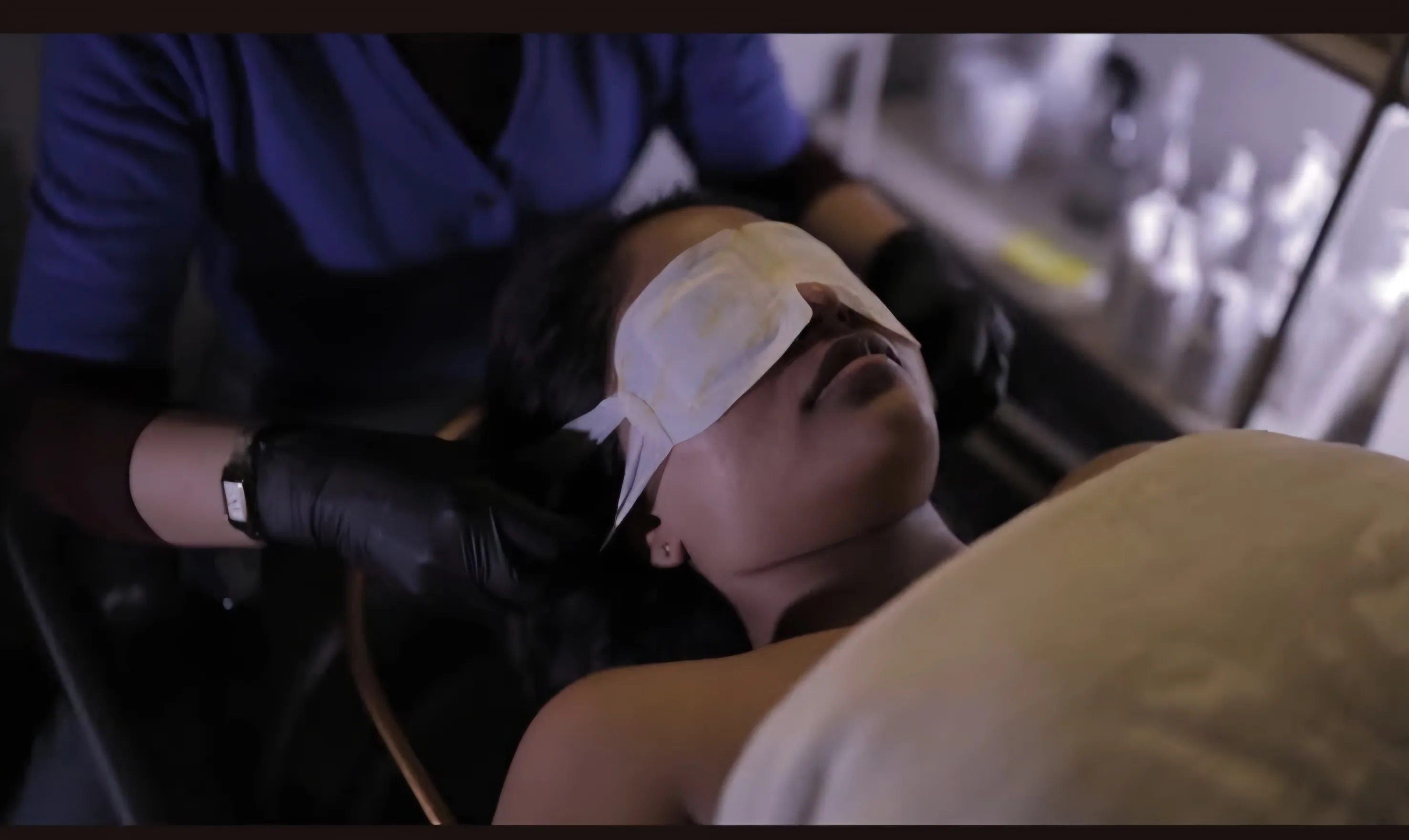 Guest reclining under a warm eye compress, therapist supporting the head during treatment